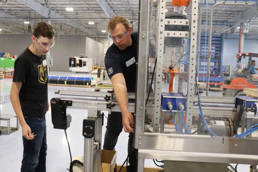 Morrison's operators director points to component on a machine to help a student build their PACK Challenge machine.